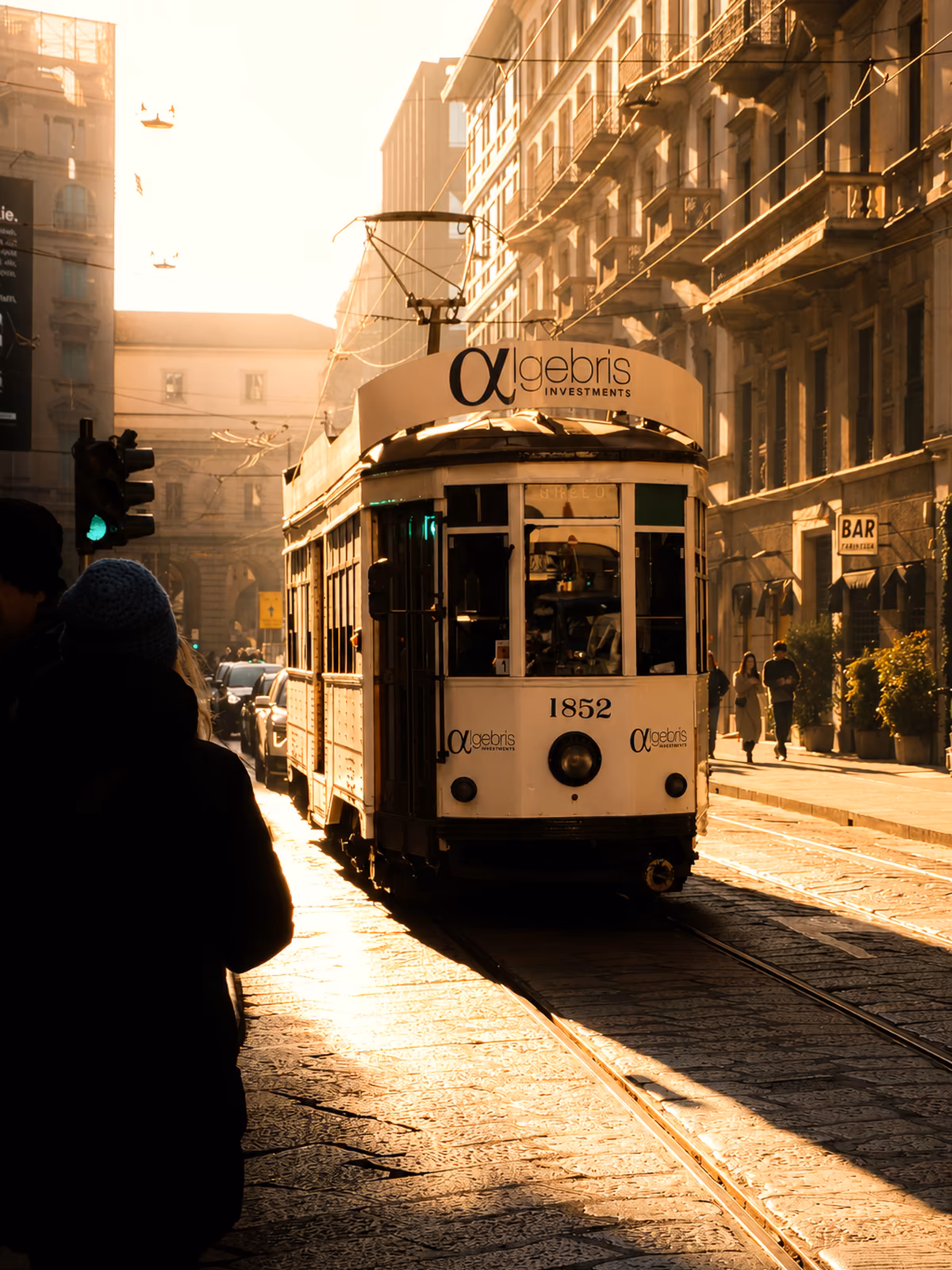 A historic Milan tram moving through a street at golden hour